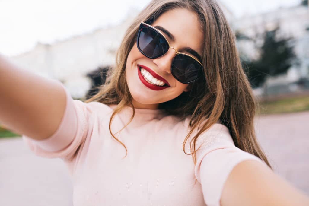 Closeup selfie-portrait of attractive girl in sunglasses with long hairstyle and snow-white smile in